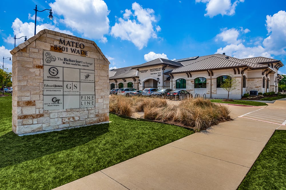 Exterior of a modern stone medical building in Frisco, TX with a prominent stone tenant monument sign on a manicured green lawn.