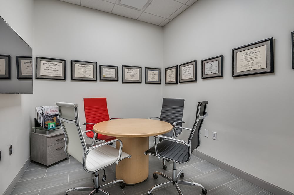 Private consultation room with a round wooden table, multi-colored leather chairs, and a wall lined with framed medical diplomas.