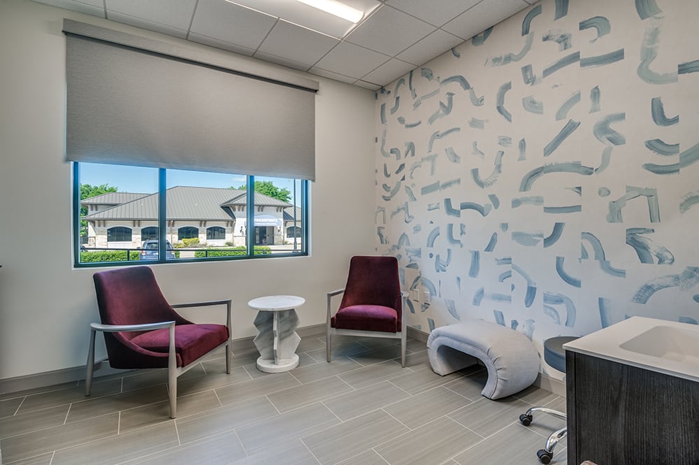 Medical examination room with a private handwashing sink station, full-length mirror, and stylish wallpaper accent.