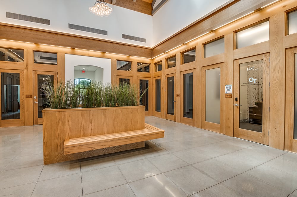 Spacious building lobby featuring warm wood paneling, floor-to-ceiling glass office entries, and a built-in wooden bench.