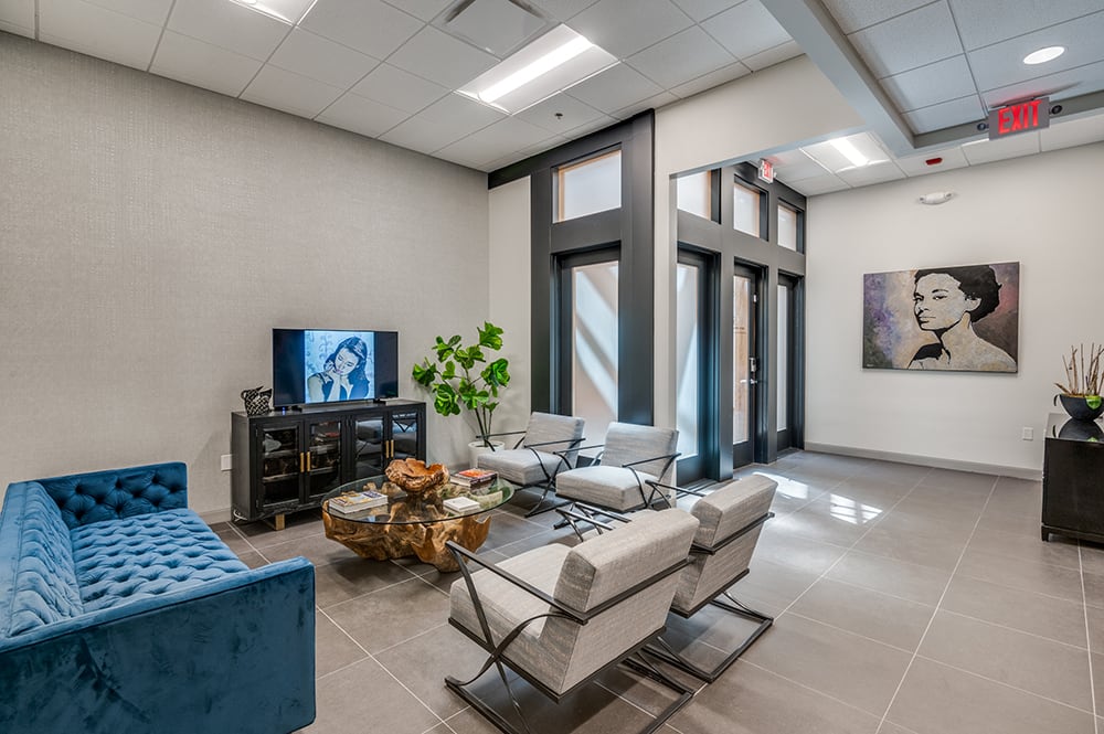 Modern patient lounge featuring a rustic raw-wood coffee table, flat-screen TV, and large windows bringing in natural light.