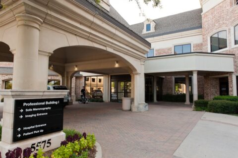 The covered driveway and main entrance of a brick medical professional building, showing a prominent black directional sign for mammography, imaging, and patient pick-up.