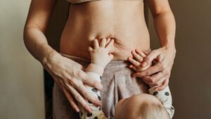 Young child reaches up and touches his mother's exposed belly.