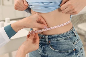 Healthcare professional measures a person’s waist with a tape measure during a health checkup.