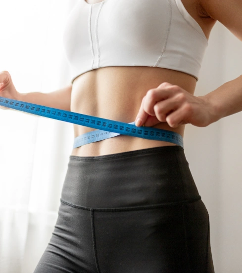 Woman measuring her toned stomach with a blue tape measure, showcasing potential body contouring and liposuction results.