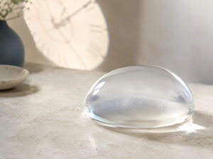 Silicone breast implant beside a clock illustrating how long breast implants last.
