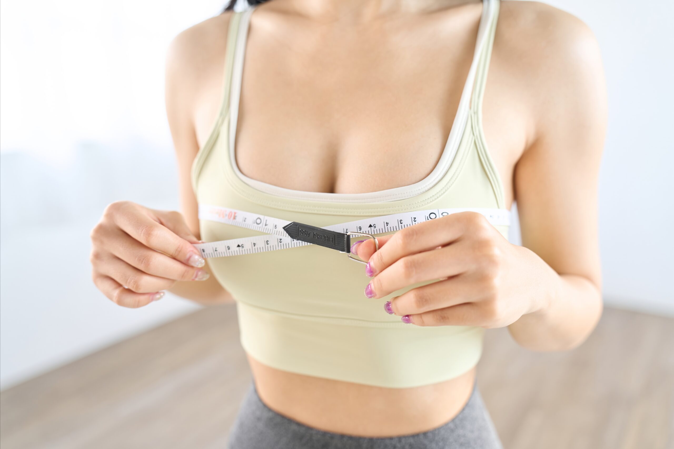 Woman measuring her breast and chest circumference while considering breast reduction surgery.
